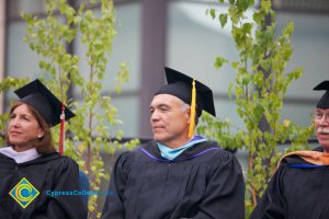 Two men and a woman in cap and gown enjoying the 48th Commencement.