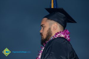 Profile of man with beard in his cap and gown and purple orchid lei.