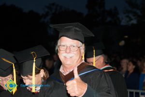 A man in cap and gown gives a thumbs up during the 48th Commencement.