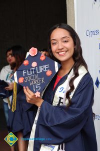 A young woman in graduation gown holding her decorated cap.