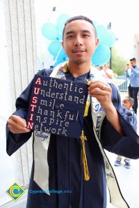 A young man in graduation gown holding his decorated cap.