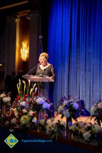 Woman wearing a black evening dress speaking on stage at the podium.