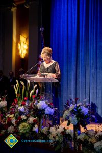 Woman wearing a black evening dress speaking on stage at the podium.