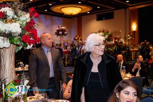 Bald man in suite and tie and woman with short grey hair and black dress turning to look at something.