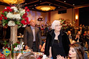 Bald man in suite and tie and woman with short grey hair and black dress turning to look at something.