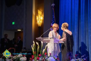 Dr. JoAnna Schilling standing at the podium with a woman in a black dress.