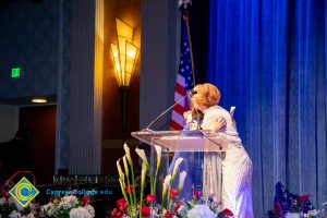 Dr. JoAnna Schilling at the podium hugging a woman in a blue dress.