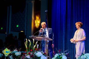 Cypress College Softball Coach, Brad Pickler speaking at the podium with Dr. JoAnna Schilling looking on.