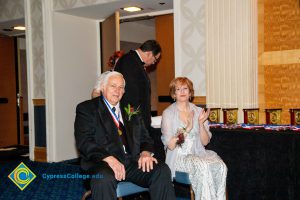 Dr. JoAnna Schilling sitting with a gentleman with a black suit and tie wearing an award around his neck.