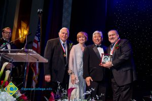 Three men in suits with Dr. JoAnna Schilling. One man is holding an award.