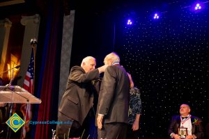 Man in suit receiving an award from another man in a suit.