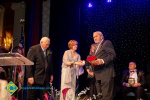 Dr. JoAnna Schilling shakes hands with an award recipient while a woman and another man look on.