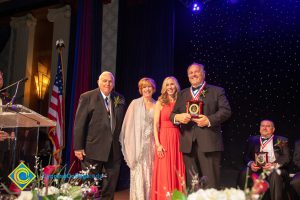 Two men in suits with awards and Dr. JoAnna Schilling and another woman in a pink dress.