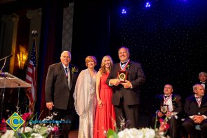 Two men in suits with awards and Dr. JoAnna Schilling and another woman in a pink dress.