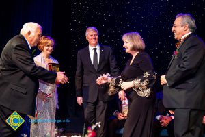 Man reaching out to shake hands with a woman in a black dress while JoAnna Schilling and two men in suits look on.