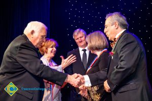 President JoAnna Schilling congratulating a woman while two men in suits shake hands and one looks on.