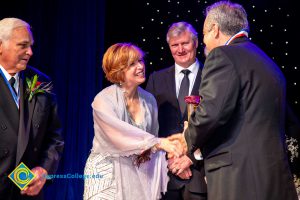 Dr. JoAnna Schilling shakes hands with an award recipient while two men look on.