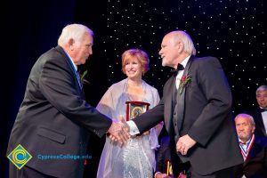 Two men in suits shaking hands while JoAnna Schilling looks on.