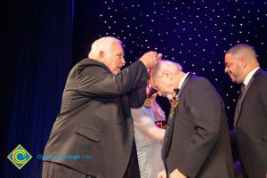 Man in a black suit presenting an award to another man.