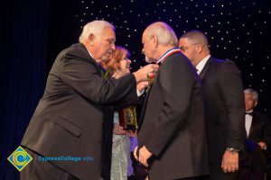 A man is adjusting an award ribbon that he presented to another man.