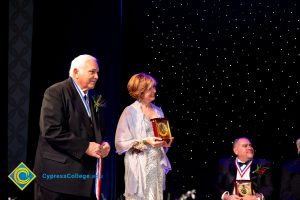 President, JoAnna Schilling holding an award with a man in a black suit standing next to her,