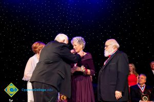 A woman in a burgundy dress receiving an award with a man in a suit standing next to her.