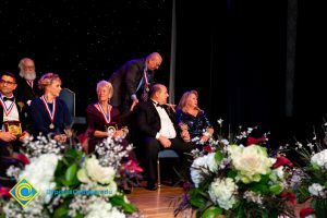 Men and women sitting on stage wearing award medals.