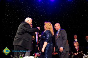 Woman in a black dress receiving an award medal while others look on.