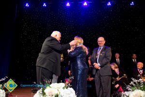 Woman in a black dress receiving an award medal while others look on.