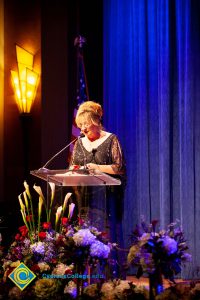 Woman wearing a black evening dress speaking on stage at the podium.