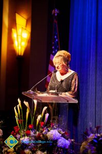 Woman wearing a black evening dress speaking on stage at the podium.