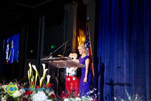 A woman in a blue dress standing on stage with Mickey Mouse.