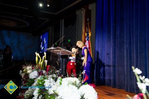 A woman in a blue dress standing on stage with Mickey Mouse.