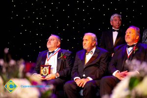 Four men in black suits and tie sitting on stage,