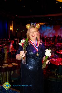 Woman wearing black and gold Mickey Mouse ears holding a vase with flowers in each hand.