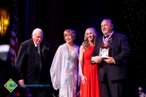 Two men in suits with awards and Dr. JoAnna Schilling and another woman in a pink dress.