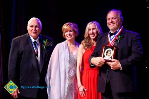 Two men in suits with awards and Dr. JoAnna Schilling and another woman in a pink dress.