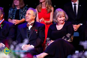 Man in sitting with hands clasped and woman in black dress looking away.