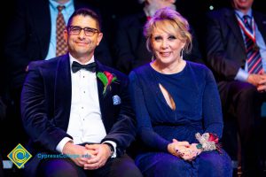 Woman in a blue dress sitting next to a man in glasses wearing a suit.