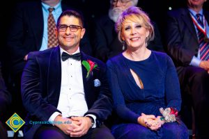 Woman in a blue dress sitting next to a man in glasses wearing a suit.