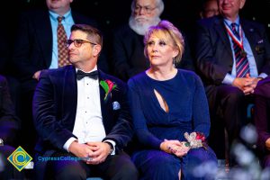 Woman in a blue dress sitting next to a man in glasses wearing a suit.