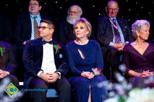 Woman in a blue dress sitting next to a man in glasses wearing a suit.