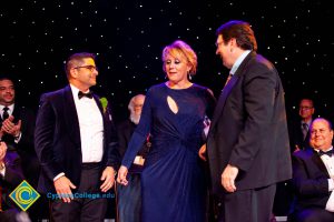 A woman in a blue dress with two men in a suits.