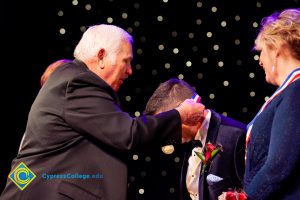 Man placing an award ribbon around another man's neck.