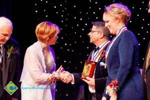 Dr. JoAnna Schilling shaking hands with a man holding an award while a woman in a blue dress looks on.