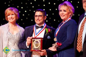 Woman in blue dress with man holding an award and JoAnna Schilling.