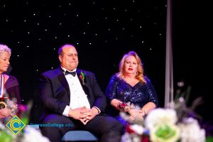 Woman in a blue dress sitting next to a man in glasses wearing a suit.