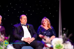 Woman in a blue dress sitting next to a man in glasses wearing a suit.