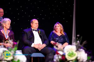 Woman in a blue dress sitting next to a man in glasses wearing a suit.