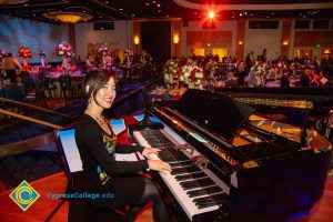 A woman dressed in black and smiling while playing the piano.